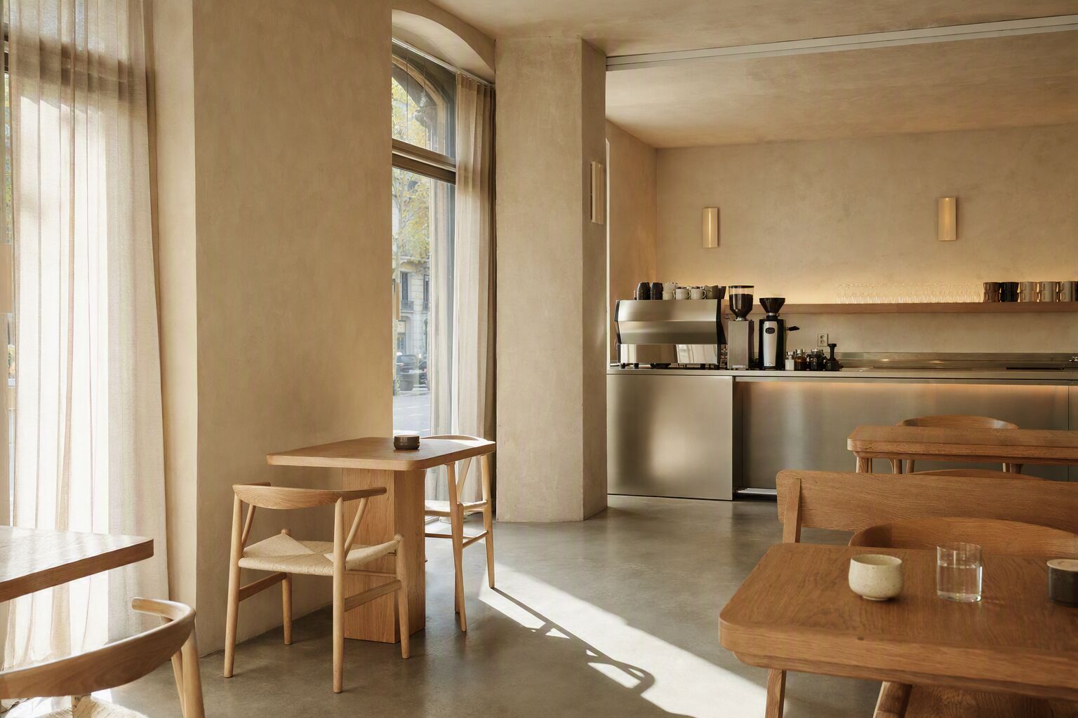 Sunlit interior of LUMA Coffee in Barcelona, with oak tables, linen curtains and a stainless steel coffee bar
